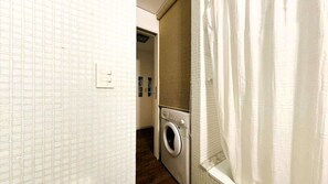 A laundry room with a washing machine, a drying rack, and a shower curtain.