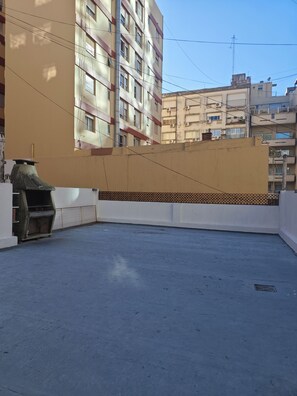 Une terrasse sur le toit, dotée d’une grille en métal, d’une bordure carrelée et offrant une vue sur les bâtiments environnants.