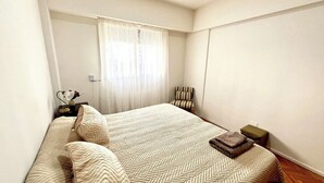 A bedroom with a large bed, a chair, a small table, and a window with curtains.