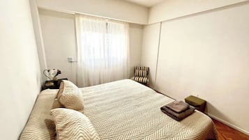 Un dormitorio con una cama grande, una silla, una mesita y una ventana con cortinas.