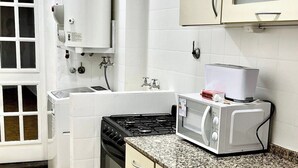 A kitchen with white cabinets, a stove, a microwave, and a water heater.