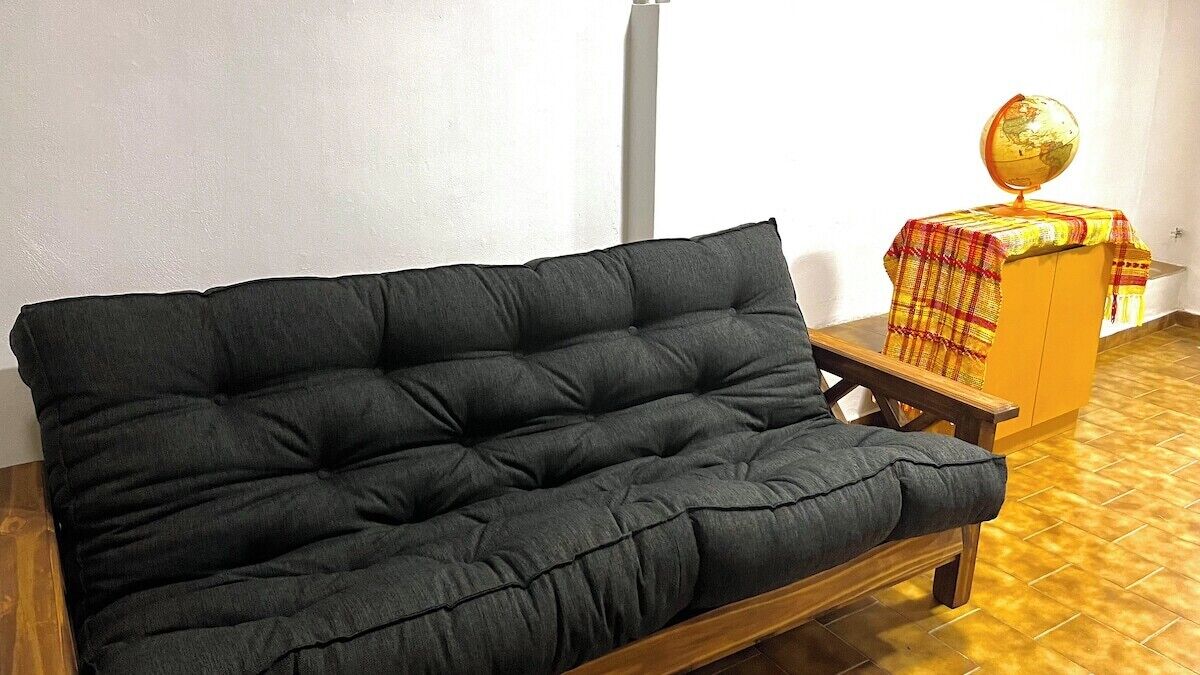 Un sofá oscuro en una habitación con piso de baldosas y una pequeña mesa de madera con un globo encima.