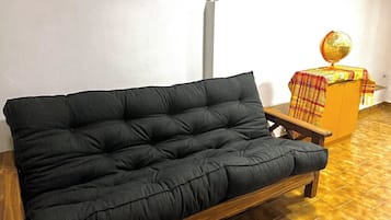 Un sofá oscuro en una habitación con piso de baldosas y una pequeña mesa de madera con un globo encima.