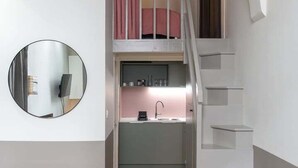 A compact living space with a kitchen area, a staircase, and a round mirror on the wall. - Lovely cozy studio - Pentes of Croix Rousse (Lyon)