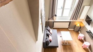 A loft-style room with a high ceiling, exposed wooden beams, a large skylight, a cozy seating area with a sofa and cushions, a small table, and a TV mounted on the wall. - Lovely cozy studio - Pentes of Croix Rousse (Lyon)