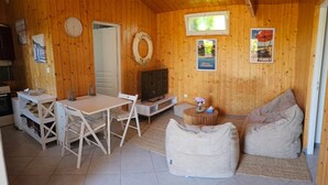 Un intérieur en bois comprenant une table à manger, des chaises, un téléviseur, un canapé et une petite table ronde sur laquelle est posé un vase de fleurs.