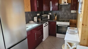 Une cuisine compacte aux murs en bois et au sol carrelé, équipée d’un réfrigérateur, d’un four à micro-ondes, d’une cuisinière et d’une petite table à manger.