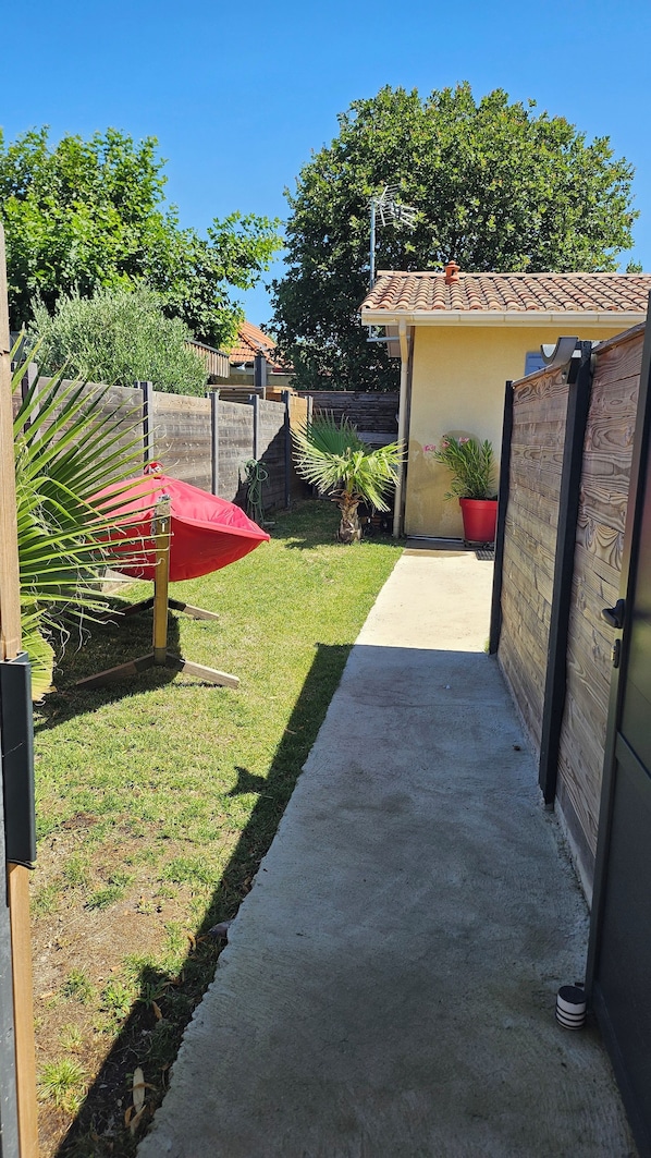 Ein schmaler Betonweg führt zu einem Haus mit einem Ziegeldach und einem Holzzaun.