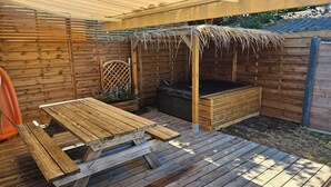 Une terrasse en bois avec un jacuzzi, une table en bois et un espace salon abrité.