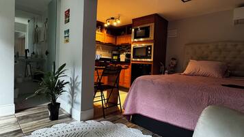 Una camera compatta con un letto, un angolo cottura e un bagno parzialmente visibile da una porta aperta.