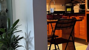 A kitchen with wooden cabinets, a coffee maker, and a microwave. There is a plant in a black pot and a chair with a cushion. - House - Studio apartment for couples in a gated community with pool, Praia do Curral in Ilhabela. (Ribeirão Ilhabela)