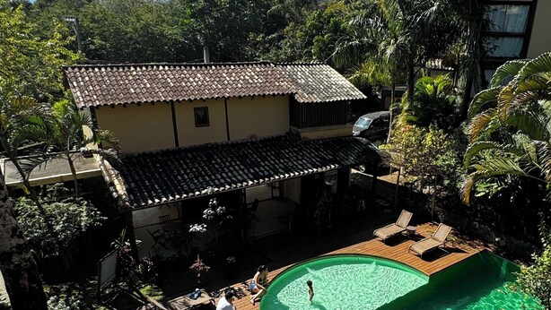 A house with a swimming pool surrounded by lush greenery and a mountain in the background. - House - Studio apartment for couples in a gated community with pool, Praia do Curral in Ilhabela. (Ribeirão Ilhabela)