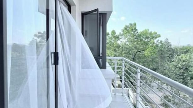 Ein Balkon mit weißem Vorhang, Glastür und Metallgeländer.
