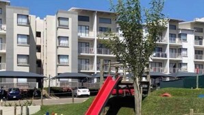 Een woongebouw met meerdere balkons, een rode glijbaan en een kleine boom op de voorgrond.