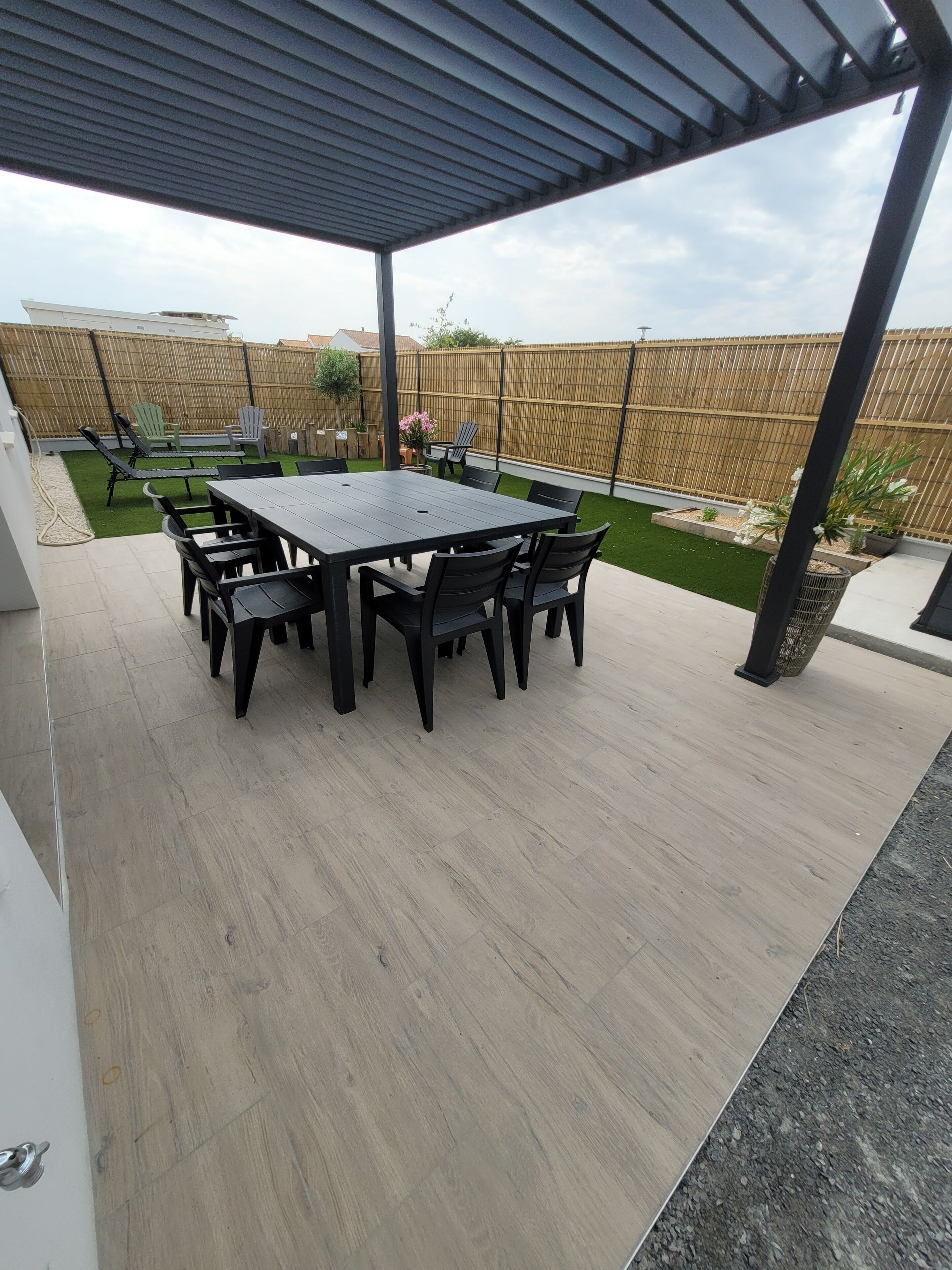 Un patio exterior con mesa y sillas cubiertas, rodeado por una valla de madera y un césped.