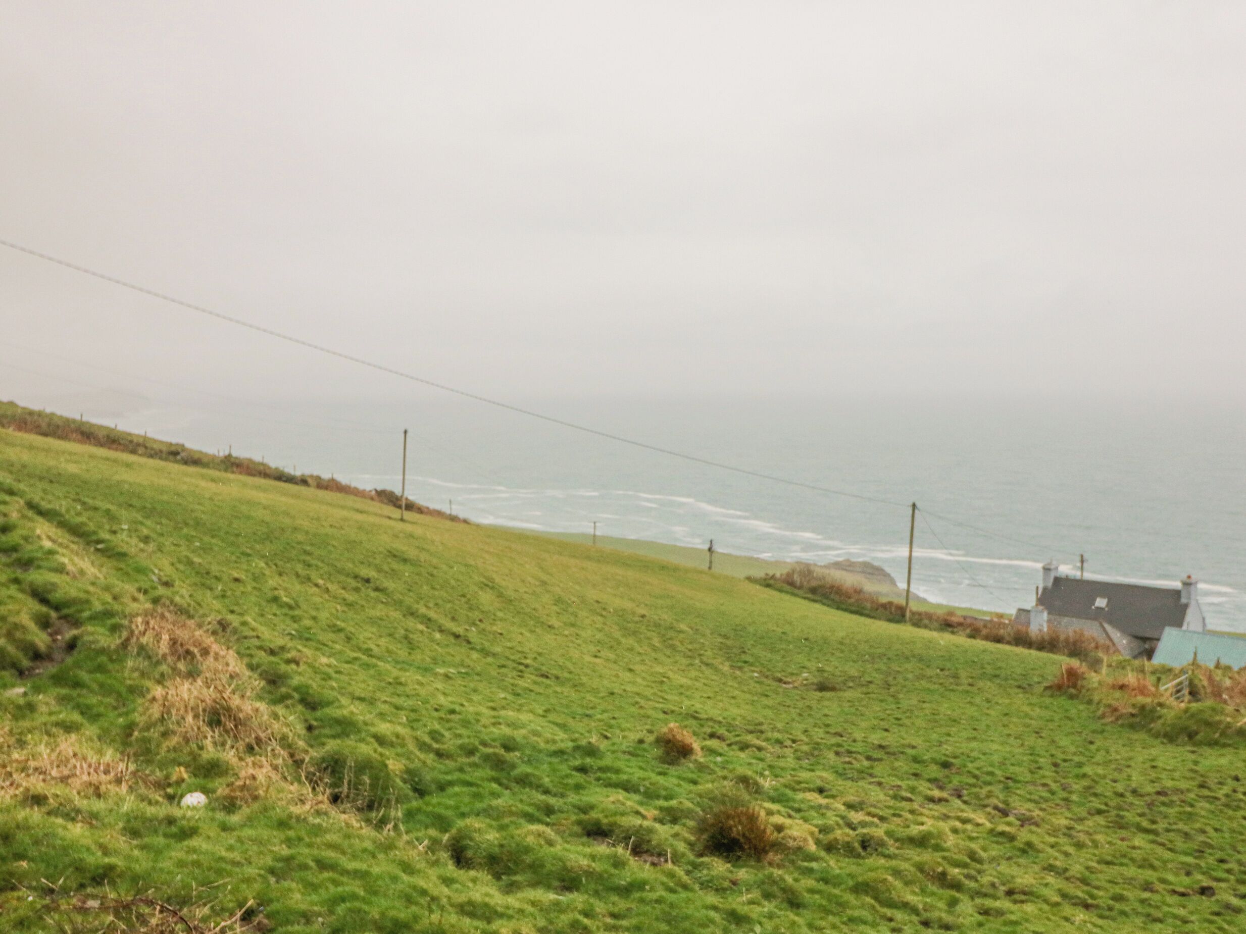 A coastal landscape with a grassy hill, a house with a sloped roof, and the ocean in the background.