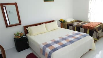 Un dormitorio con una cama grande, una mesita de noche con un florero, una silla, una pequeña mesa con un arreglo floral y un espejo en la pared.