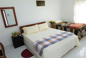 Ein Schlafzimmer mit einem großen Bett, einem Nachttisch mit Blumenvase, einem Sessel, einem kleinen Tisch mit Blumen und einem Spiegel an der Wand.