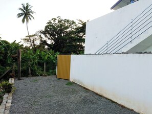A gravel driveway leading to a white wall with a wooden gate. - Tropical Suites (Negombo)