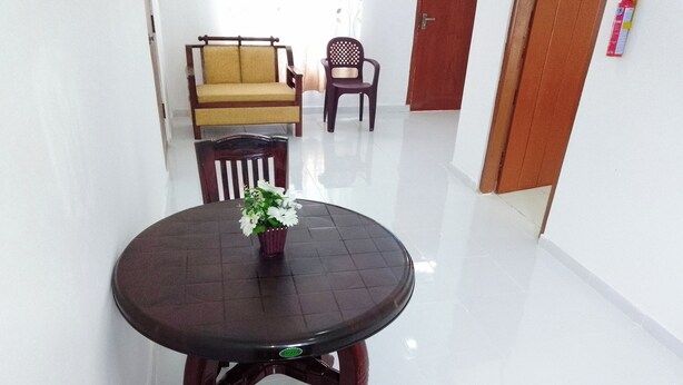 A dining area with a round table, chairs, a sofa, and a chair with a perforated backrest. - Tropical Suites (Negombo)