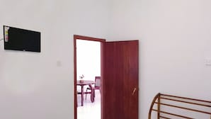 A room with a white wall, a wooden door, a small table with a chair, and a bed with a wooden frame. - Tropical Suites (Negombo)