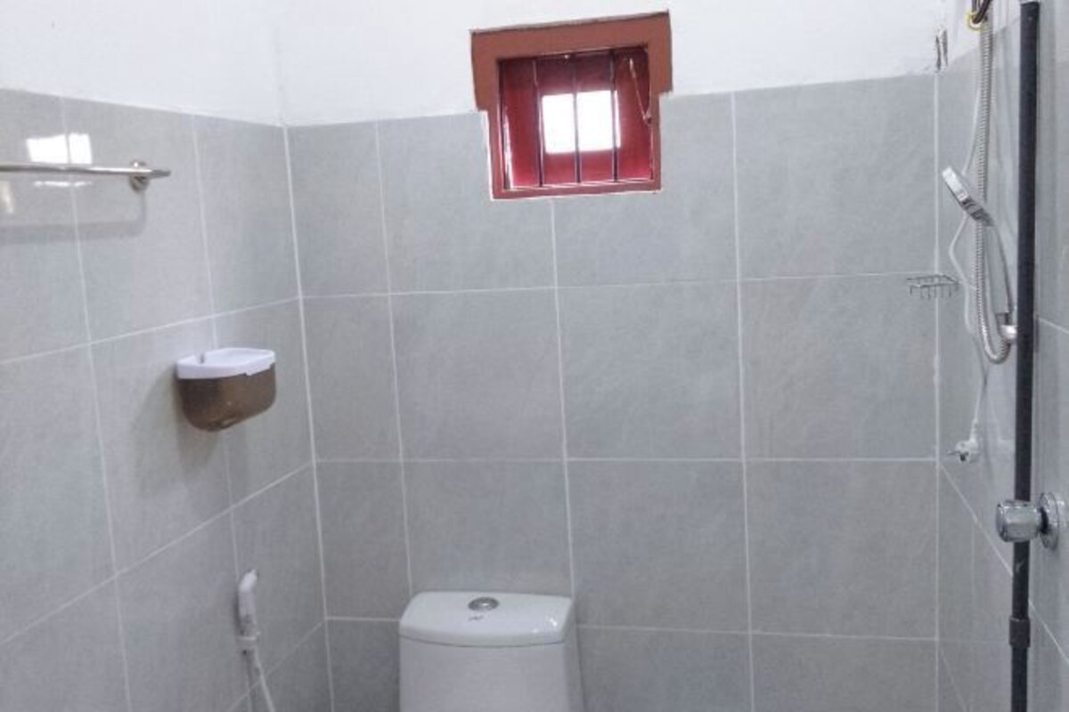 Egy kis, csempézett fürdőszoba, amelyben WC, zuhanyzó és egy ablak található.