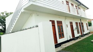 A white building with a balcony, multiple windows, and a small garden area. - Tropical Suites (Negombo)