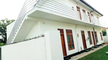 A white building with a balcony, multiple windows, and a small garden area.