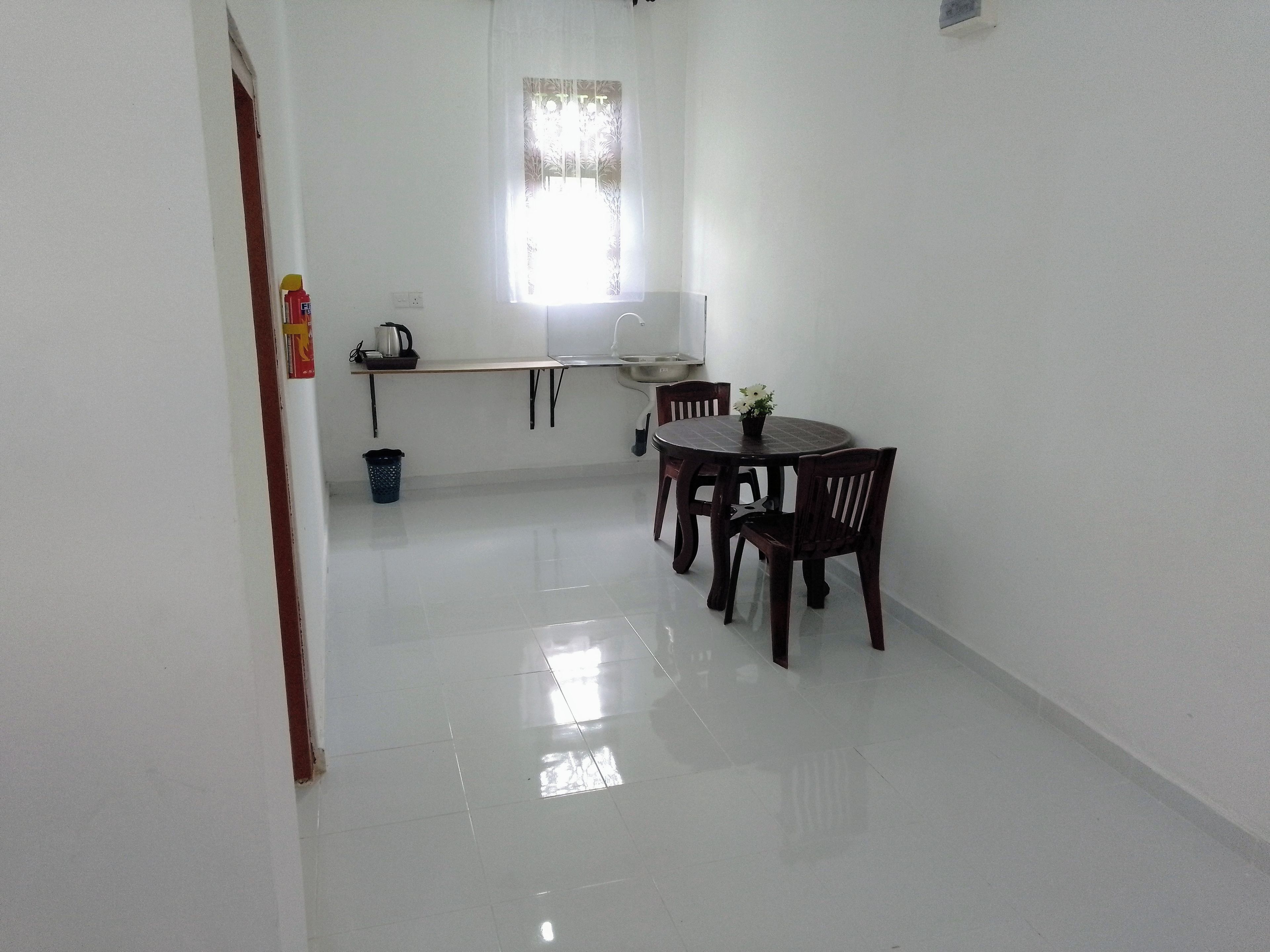 Una habitación limpia con paredes blancas, una mesa de comedor y sillas, un ventanal pequeño y un cubo de basura.
