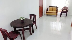 A room with a round table, two wooden chairs, a yellow sofa, and a plastic chair. - Tropical Suites (Negombo)