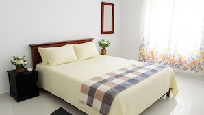 A neatly made bed with a checkered blanket, a wooden headboard, and two bedside tables with potted plants. - Tropical Suites (Negombo)