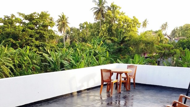 A rooftop terrace with a table and chairs, surrounded by lush greenery and a white wall. - Tropical Suites (Negombo)