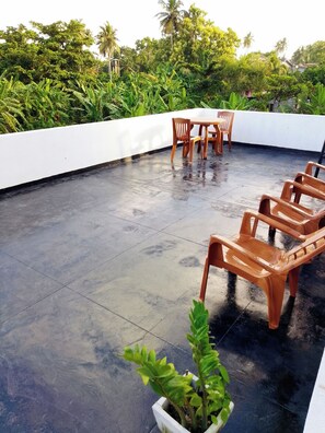 A rooftop terrace with a table and chairs, surrounded by lush greenery and a white wall. - Tropical Suites (Negombo)
