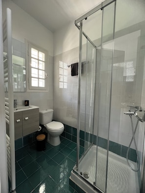 A bathroom with a shower, toilet, sink, and a window.