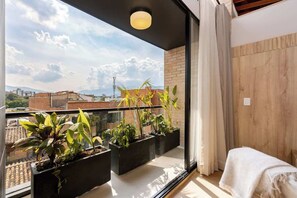 En balkon med krukker med planter, udsigt til bygninger og en trævæg.