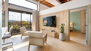 A modern living room with a large TV, wooden flooring, and a balcony with plants. - Digital Nomad Paradise 1BR Luxury & Peace with A/C (Medellín)