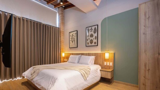 Une chambre moderne avec un grand lit, une tête de lit en bois, des tables de chevet avec des lampes et des œuvres d’art accrochées aux murs.