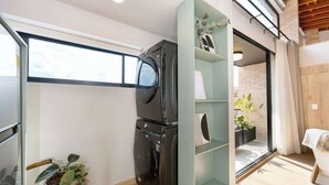 A compact room with a washing machine, a small plant, and a glass shelf unit. - Digital Nomad Paradise 1BR Luxury & Peace with A/C (Medellín)
