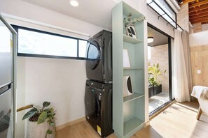 A compact room with a washing machine, a small plant, and a glass shelf unit.