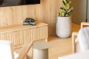 Un salon moderne avec un banc en bois, une plante en pot et un téléviseur à écran plat fixé au mur.