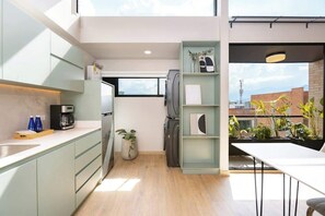 Une cuisine moderne avec un plancher en bois clair, un four encastré et une machine à café. Une fenêtre laisse entrer la lumière naturelle et offre une vue sur la ville.