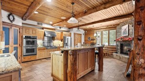 A spacious kitchen with wooden cabinets, a large island, and a stone fireplace.