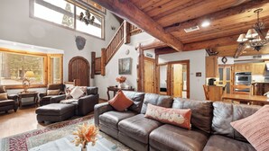 A spacious living area with a leather sofa, wooden staircase, and a kitchen in the background.