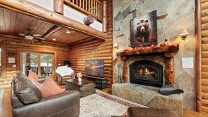 A log cabin interior with a fireplace, leather furniture, and a stone wall.