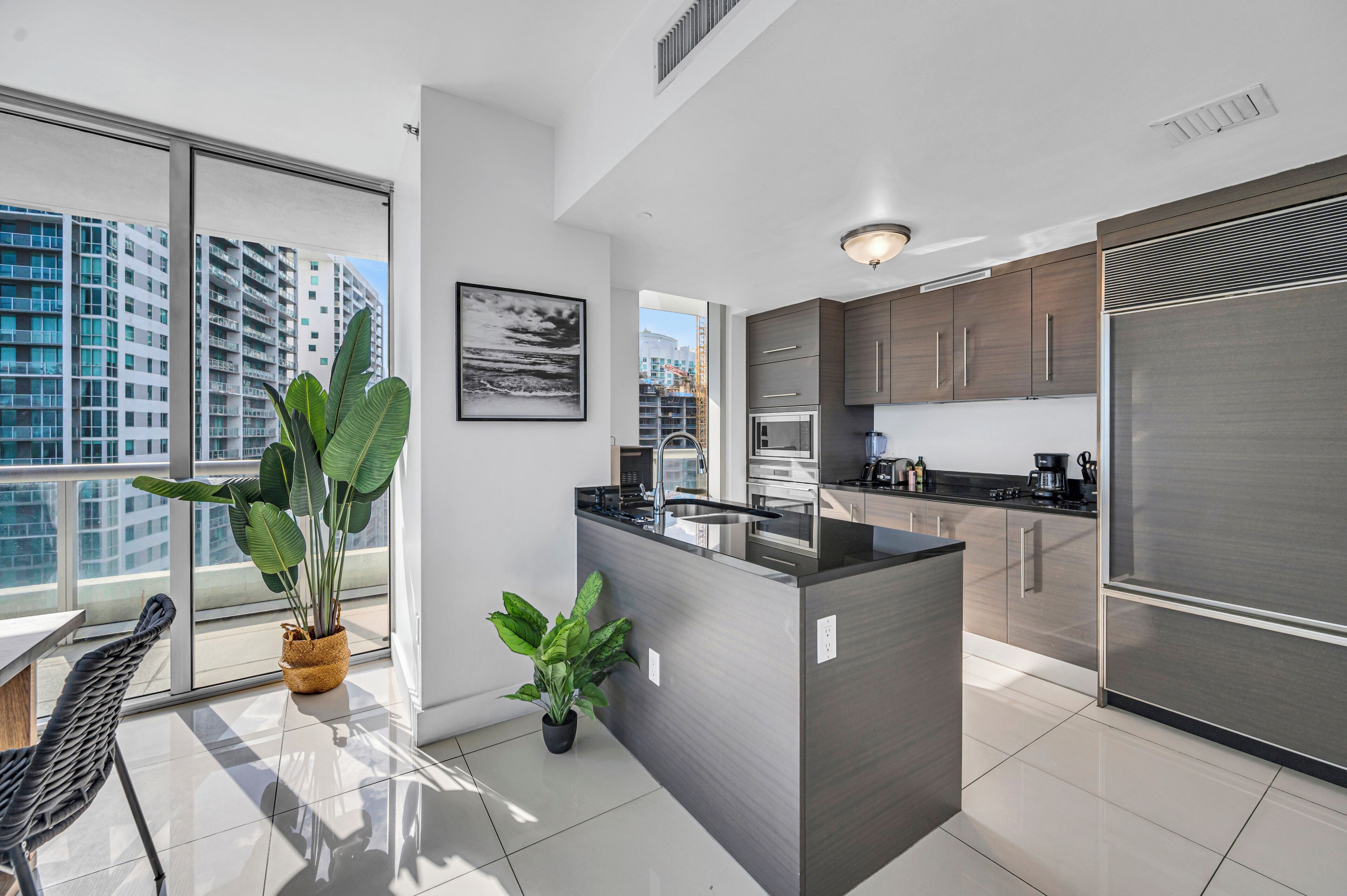 A modern kitchen with a central island, stainless steel appliances, and large windows offering a city view.
