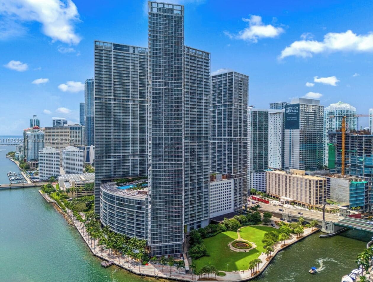 A high-rise building with a modern glass facade, surrounded by water and greenery.