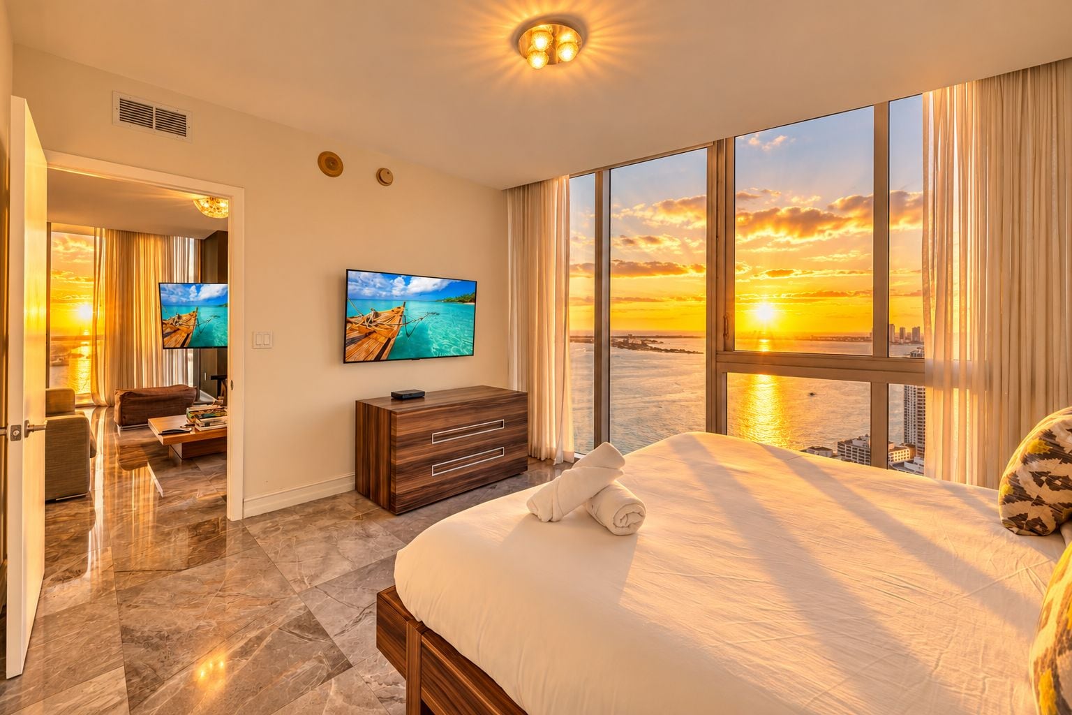 A hotel room with a large bed, a TV, a view of the sunset, and a cityscape.