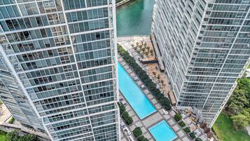 A high-rise building with a swimming pool, surrounded by greenery and a body of water.