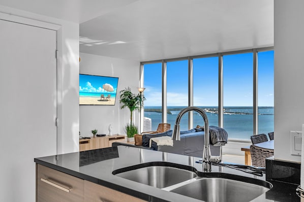 A modern kitchen with a large window overlooking the sea, a built-in sink, and a dining area with a view.