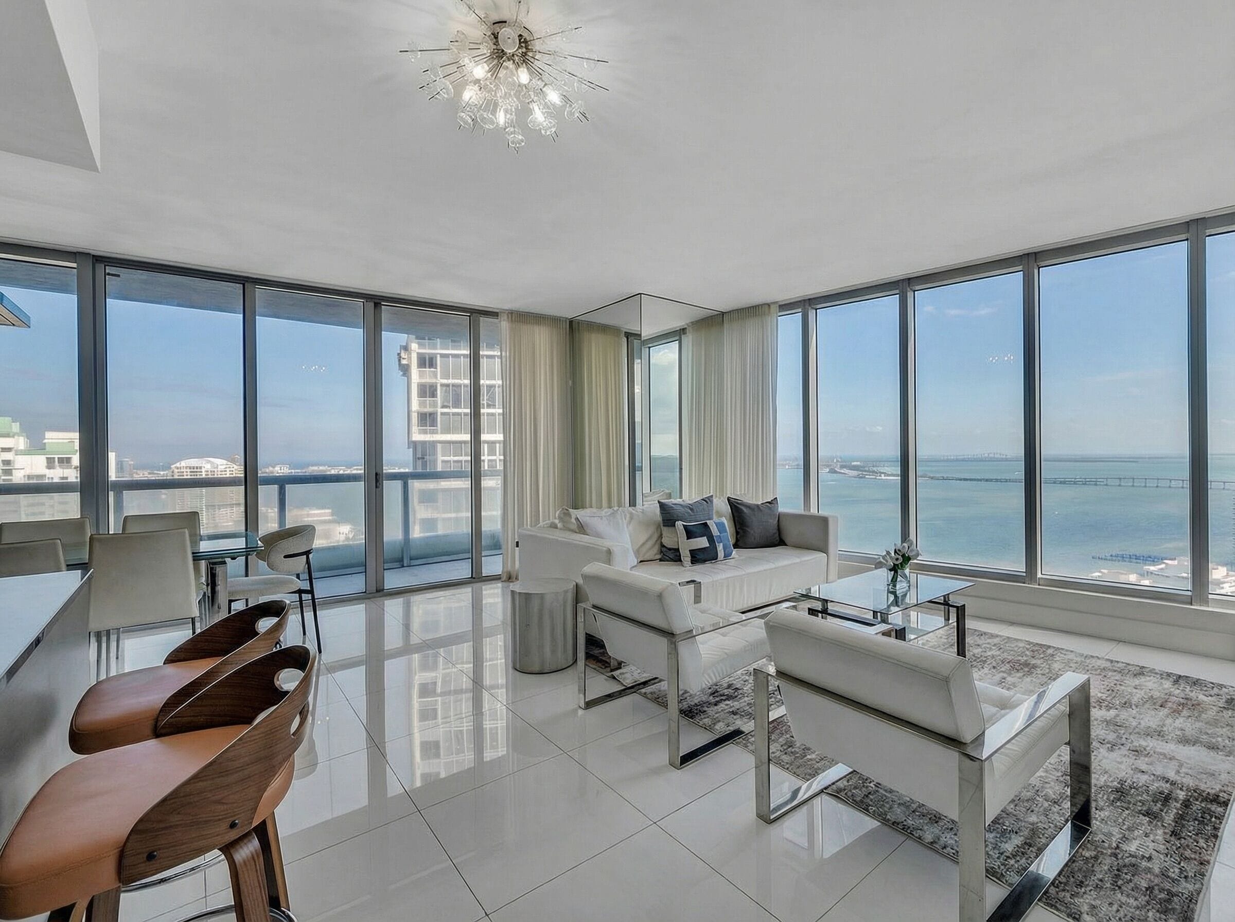 A spacious living room with a large window, a white sofa, a coffee table, and a dining area with chairs.